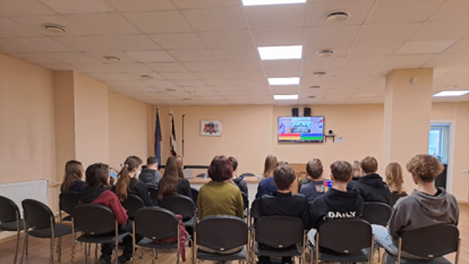Attēlā attļeoti skolēni, kas seiž telpā uz krēsliem.