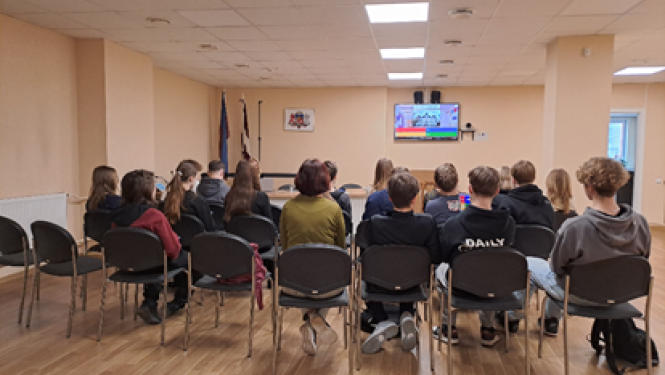 Attēlā attļeoti skolēni, kas seiž telpā uz krēsliem.