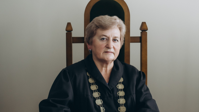 Attēlā tiesnese sēž tiesas zālē