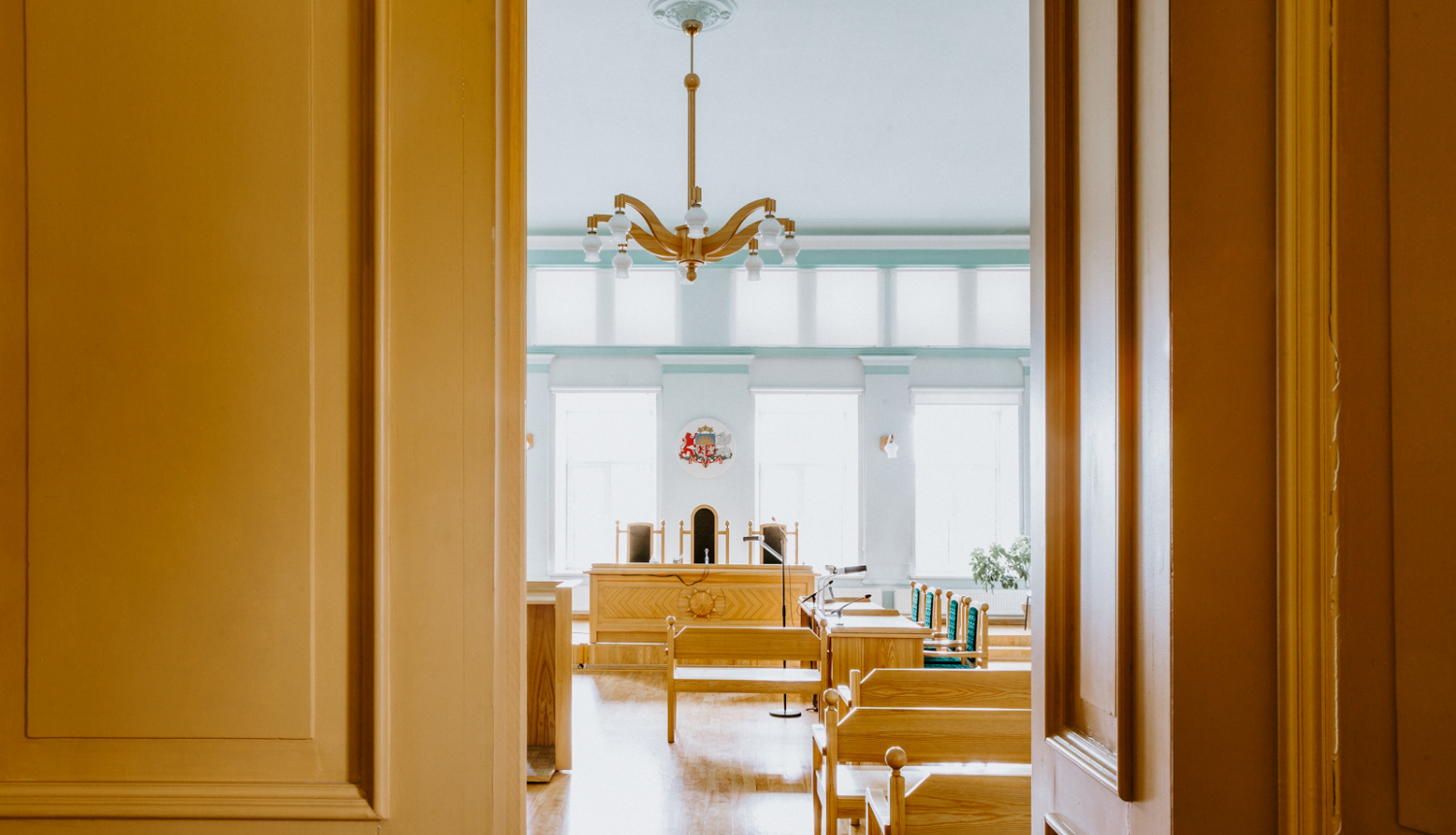 Attēlā redzamas atvērtas durvis, kur tālāk ir tiesas zāle